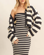 Woman wearing a black and white striped dress with a matching cardigan on a beige background
